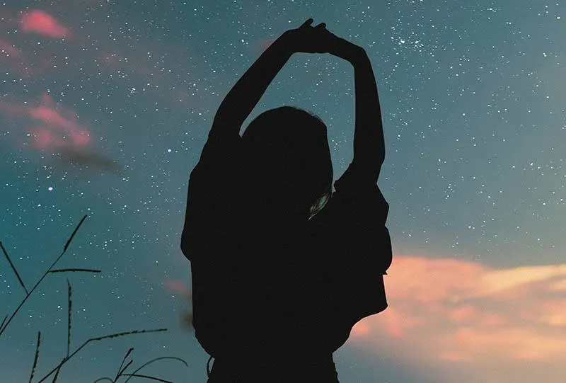 silhouette of woman raising her hands up to stars