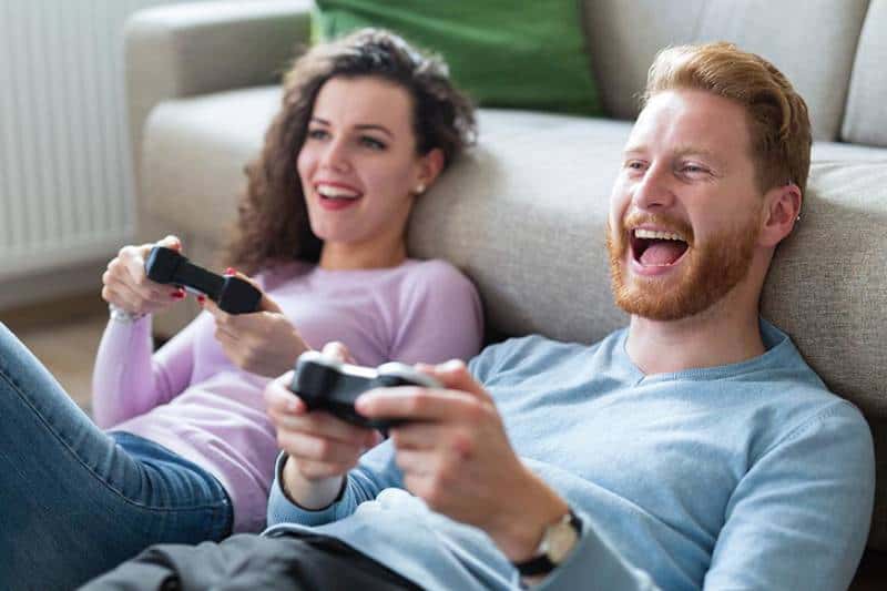 pareja sonriente sentada en el suelo y jugando a la videoconsola