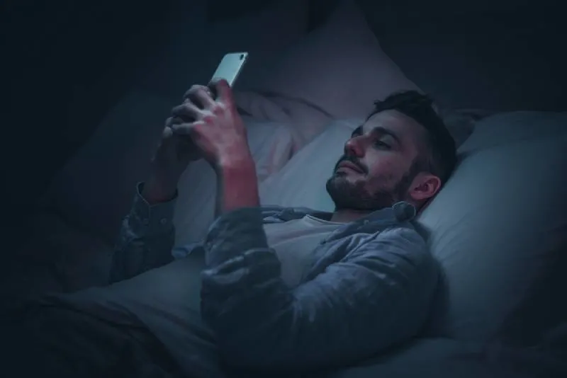 smiling man using smartphone before bed