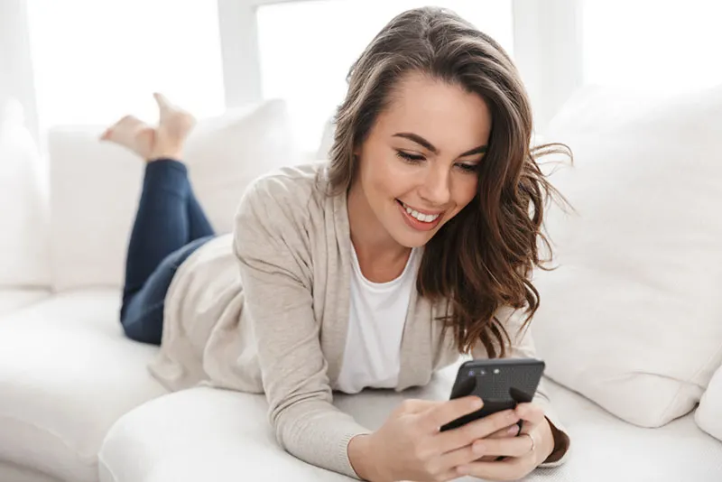 smiling woman lying on the couch and texting