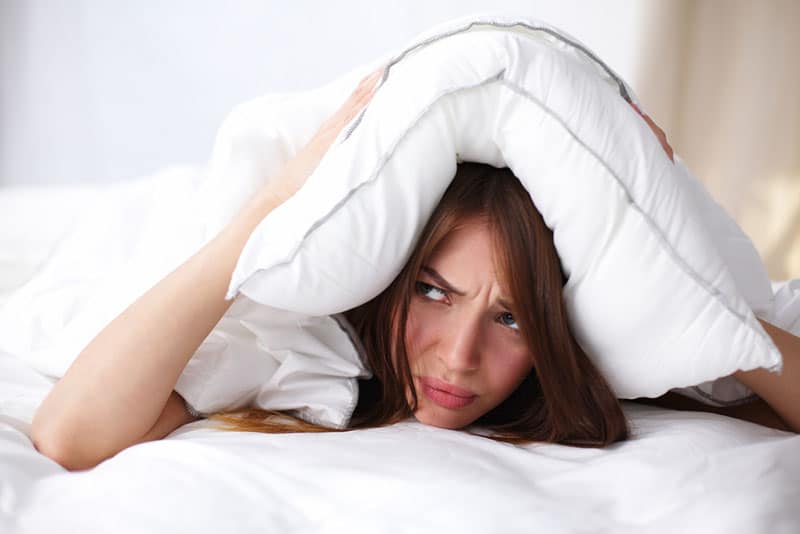 mujer disgustada poniéndose una almohada en la cabeza