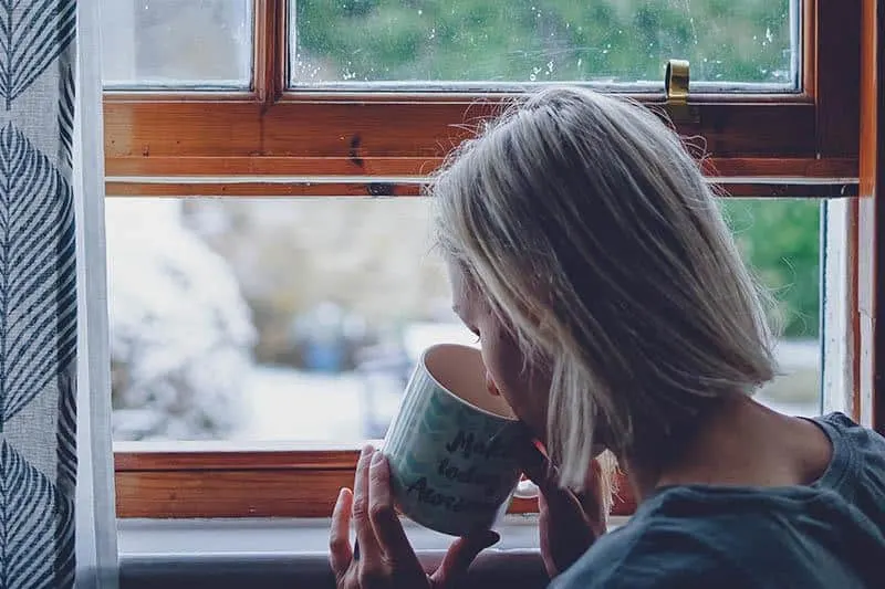 woman drinking tea beside window at home