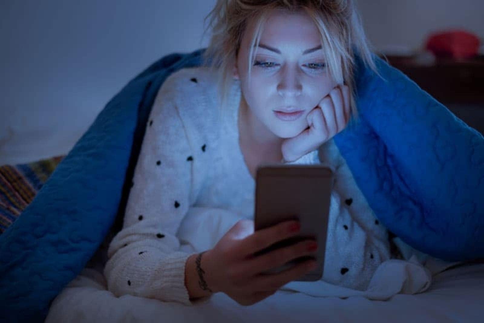 woman lying on the bed under the quilt key on the phone