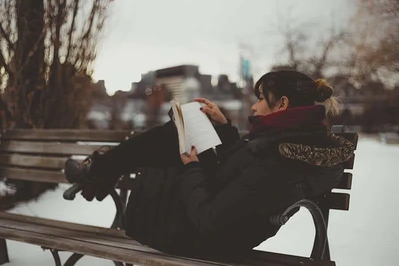woman reading book while sitting on a park bench