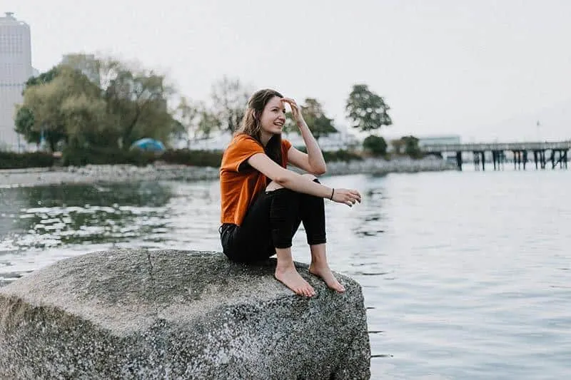 woman sitting on rock beside lake