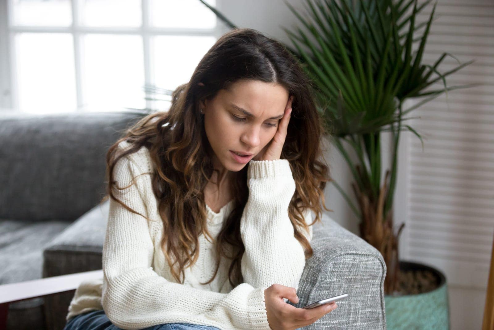 worried woman texting on phone in the living room