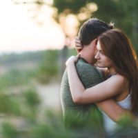 outside in nature, a brunette and a man in a green T-shirt are hugging