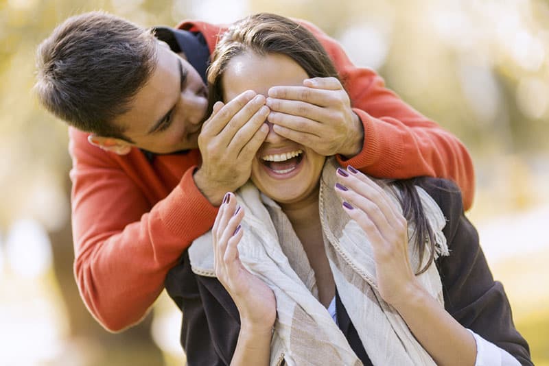 happy man putting hands on woman eyes