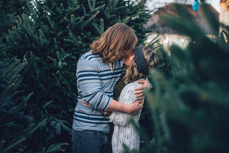 Man kisses woman near pine tree