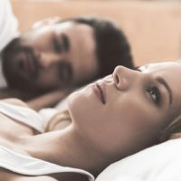 mulher preocupada deitada na cama ao lado do namorado