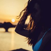 side view of shallow focus of woman in bikini standing by the water during golden hour