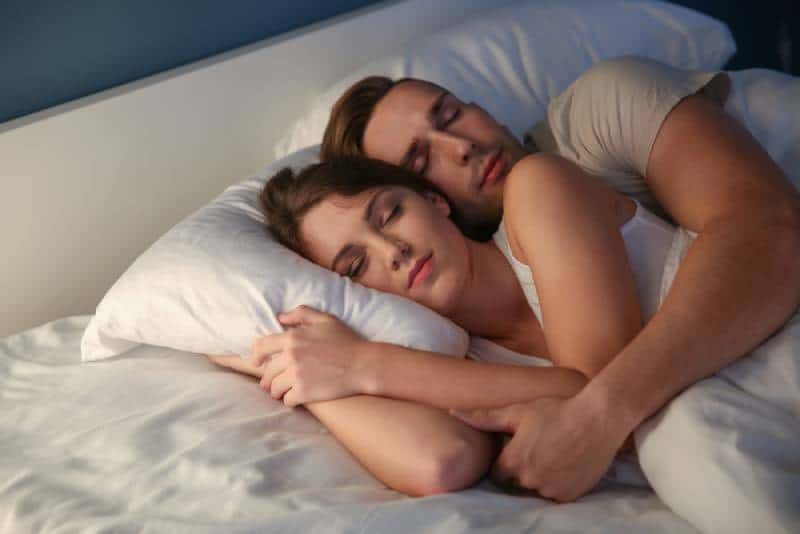man hugs woman while sleeping together in bedroom