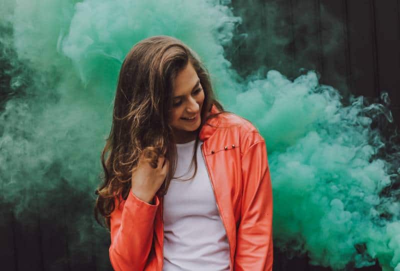 Woman wearing orange leather jacket surrounded by green smoke