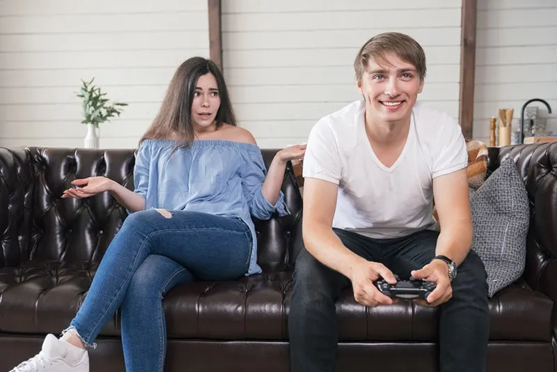 annoyed woman sitting next to man who playes games