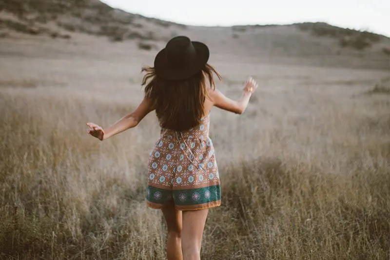 back view of girl wearing hat and walking on field