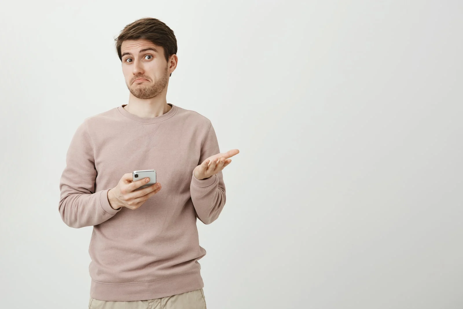 confused man looking at camera while holding a phone
