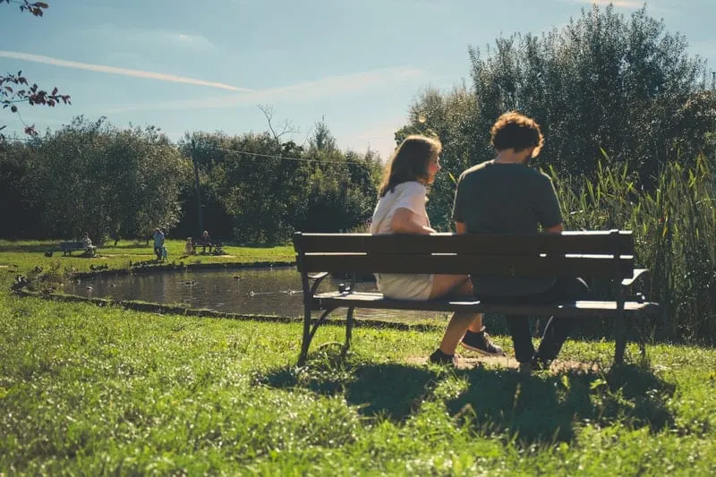 couple sitting in front of lake on a park bench