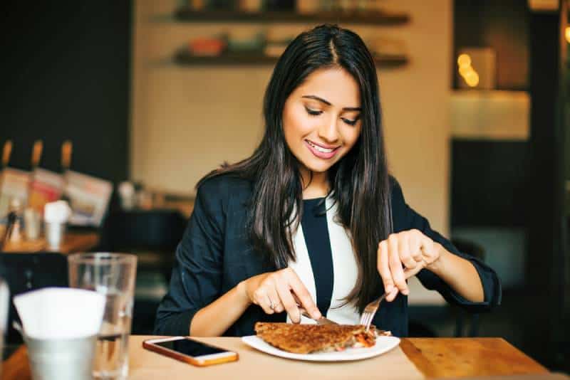 mulher jovem e feliz a comer uma panqueca num restaurante