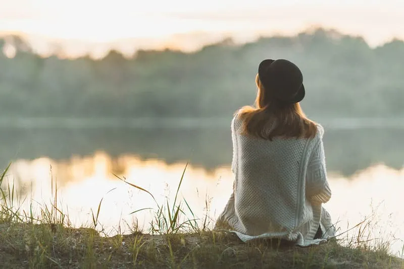 lonely woman sitting on the grass by the lake