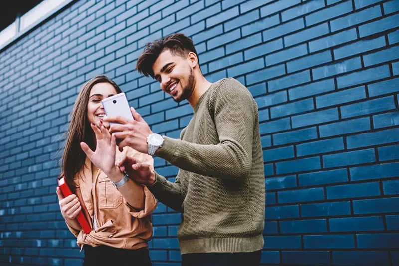 man showing phone to woman outside