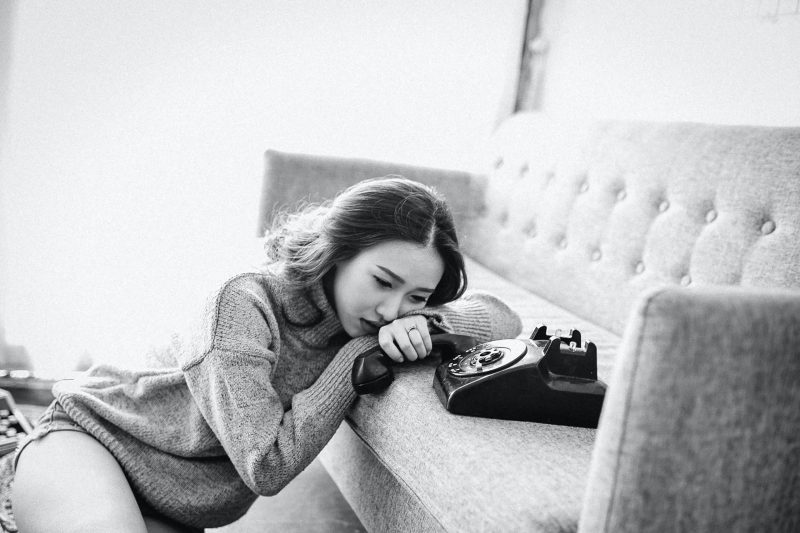 sad woman holding phone while leaning on sofa