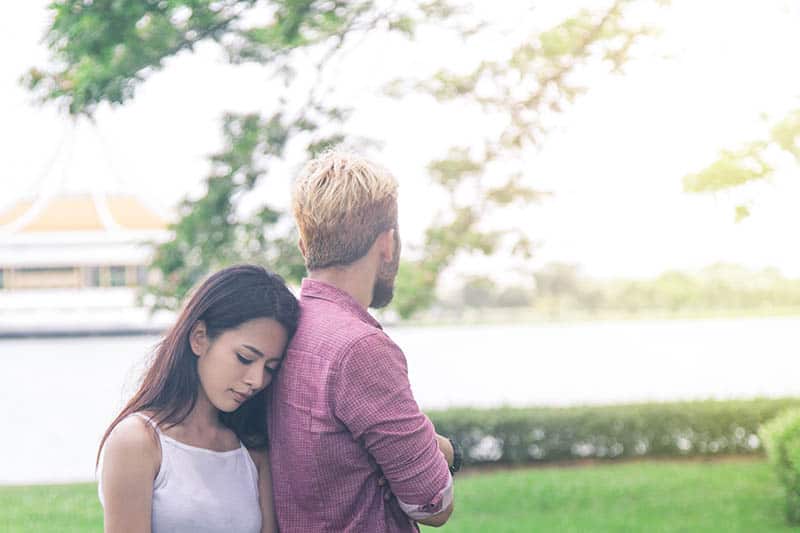 thoughtful woman puts head on man back while standing outside