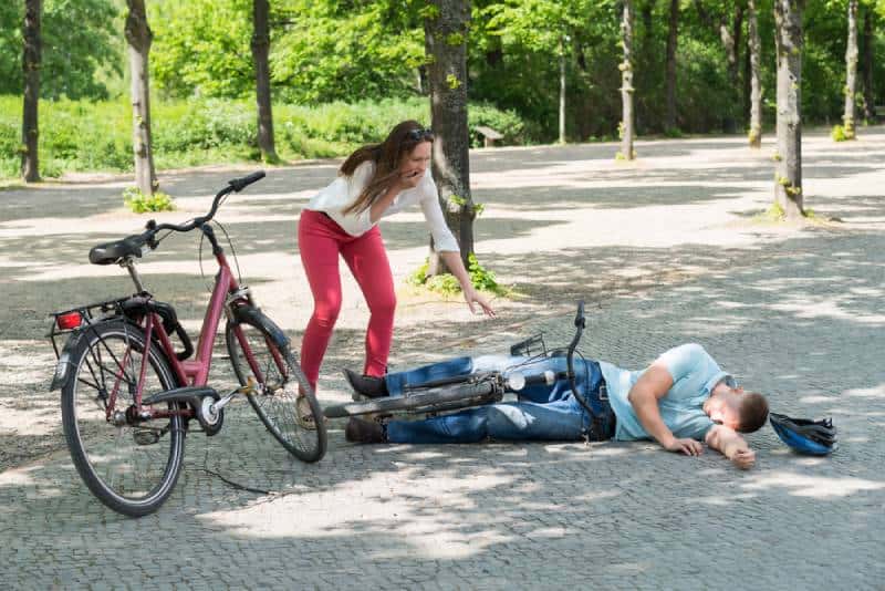 worried woman looking at man falling down while diring bicycle