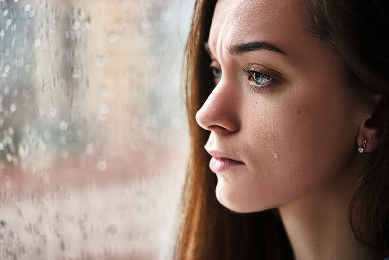 young woman crying by the window