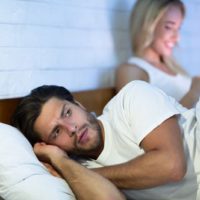 jealous man laying next to woman in bed