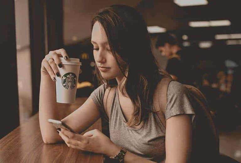woman typing on her phone while holding cup of coffee