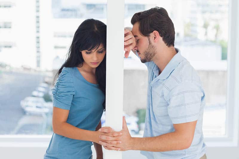 unhappy couple holding hands while leaning on wall