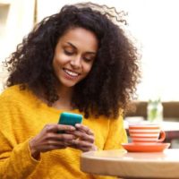 donna afro sorridente che scrive al telefono in un caffè