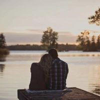 back view of romantic couple sitting in front of lake