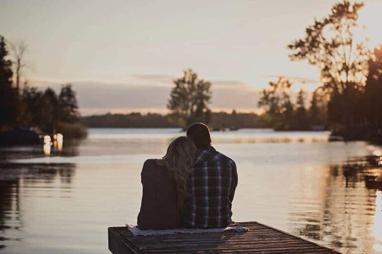 back view of romantic couple sitting in front of lake