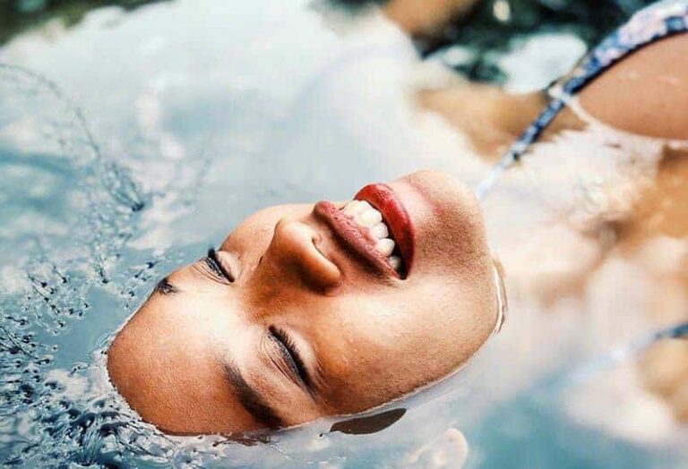 close up photo of smiling woman face lying on water