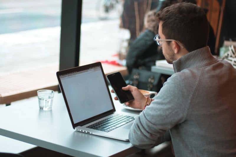 Hombre sentado cerca de una mesa con portátil y smartphone cerca de una ventana