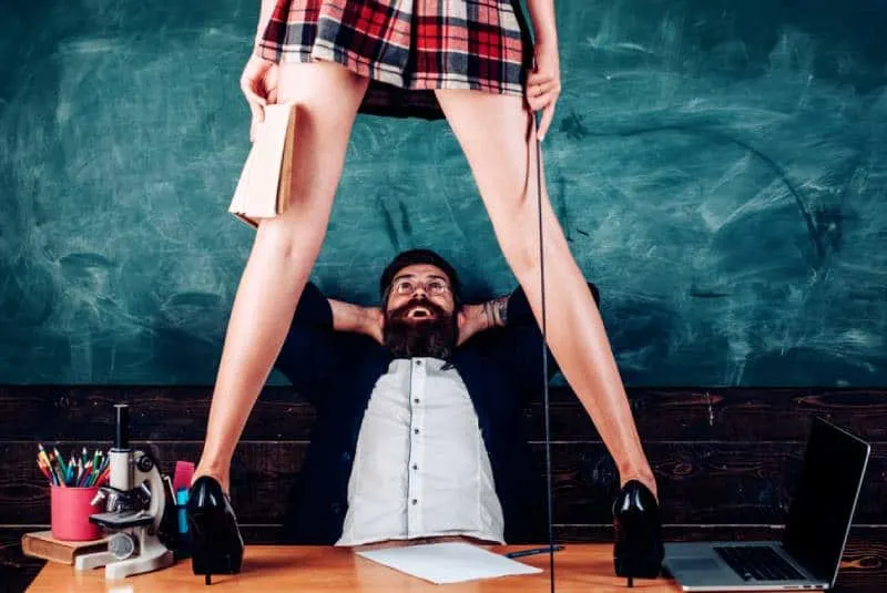 bearded man sitting on chair while woman standing on table in mini skirt