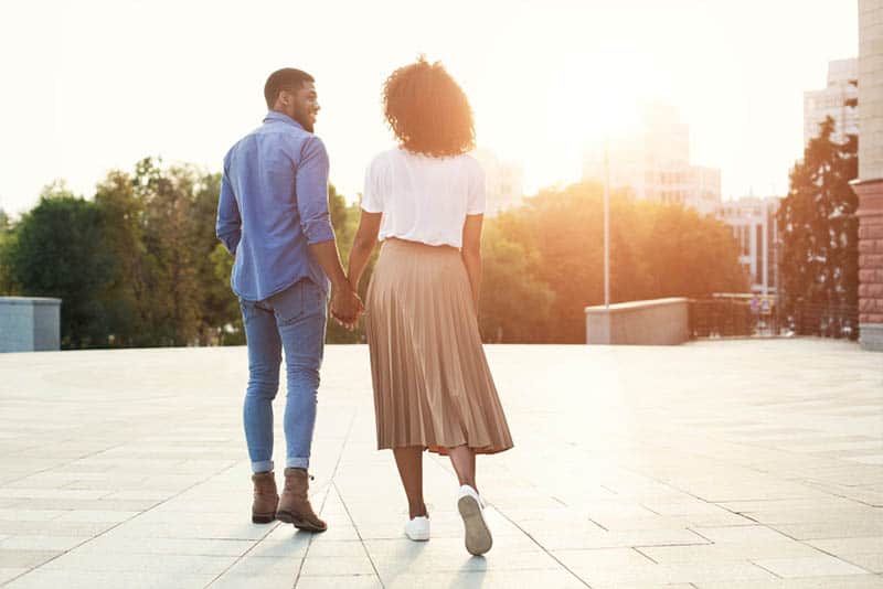 pareja cogidos de la mano y caminando durante la puesta de sol