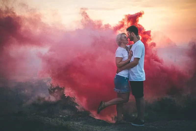 couple kisses beside red smoke outside