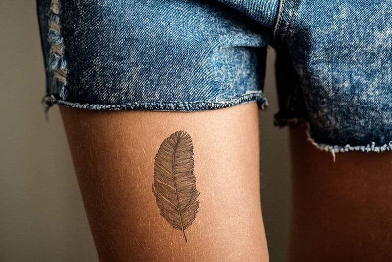 tatuaggio piuma su gamba femminile