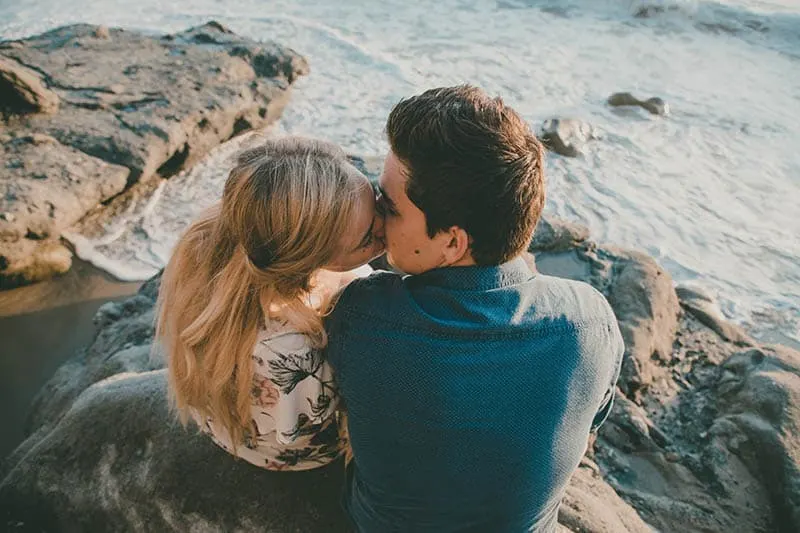 high angle of couple kissing on rocks in front of sea