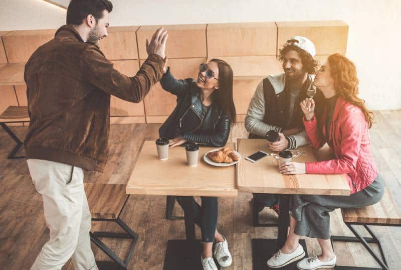 hombre y mujer alegres chocando los cinco mientras se encuentran en un café