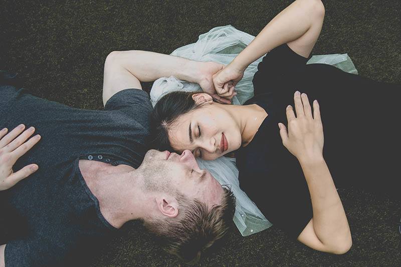 bella coppia sdraiata sull'erba con il viso rivolto l'uno verso l'altro occhi chiusi