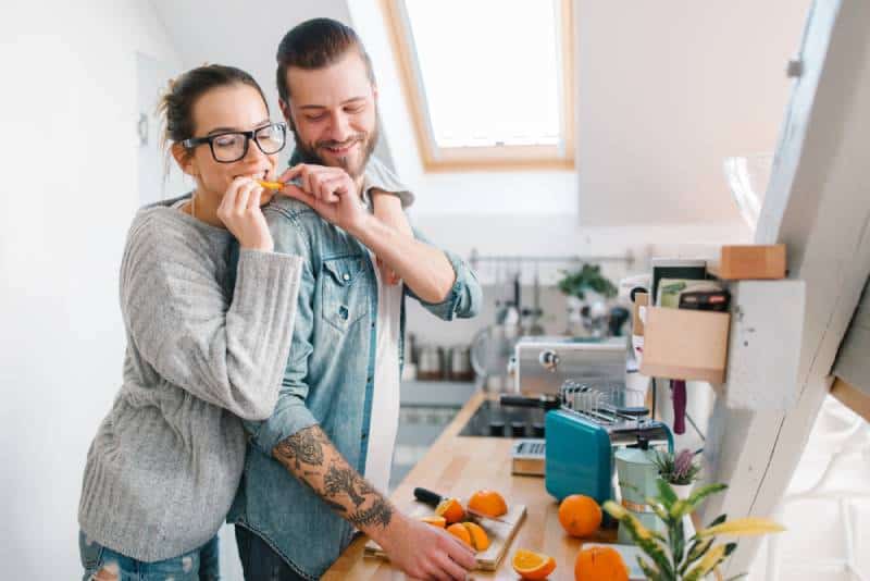 hombre dando trozo de naranja a su novia en la cocina