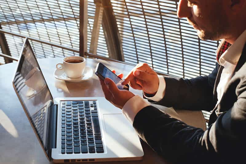 uomo in giacca e cravatta seduto al bar che scrive sul suo cellulare