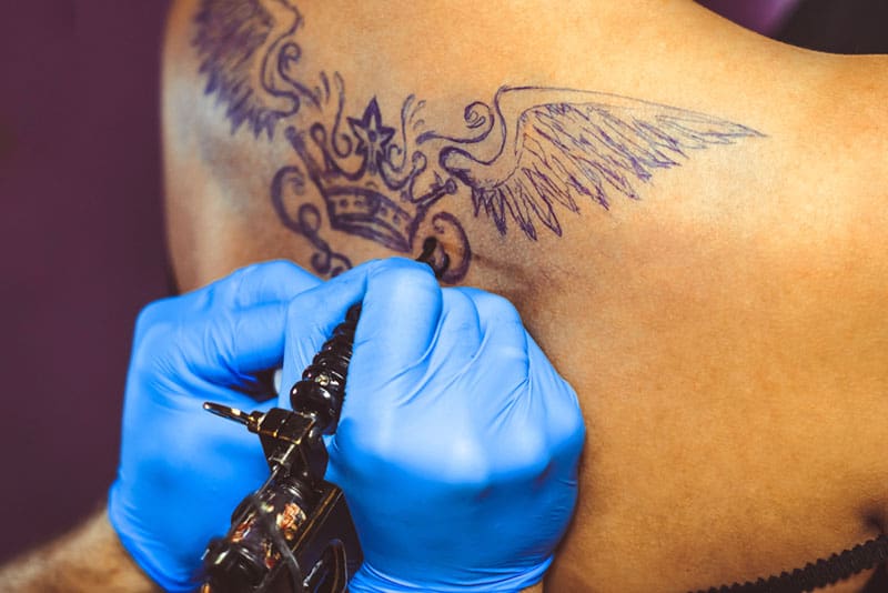man tattooing a crown on womans body