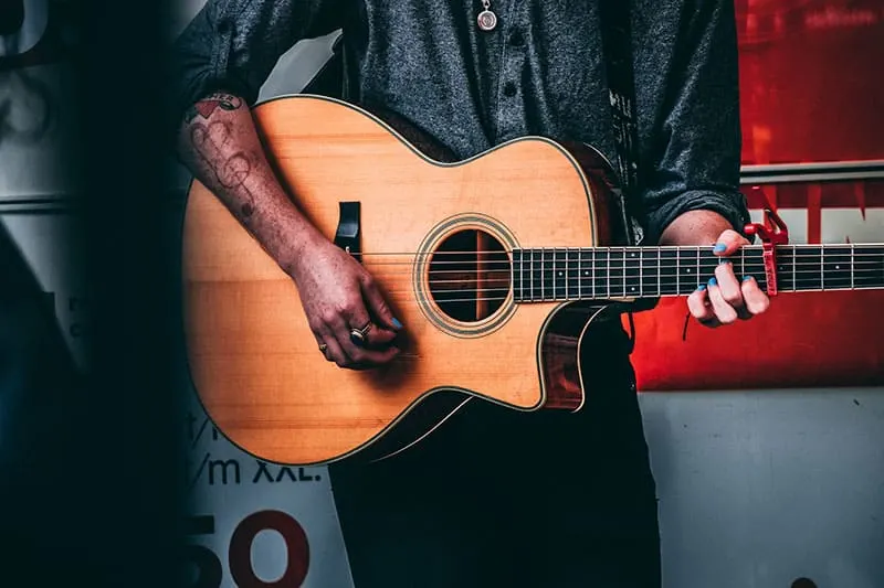 man with clef tattoo playing a guitar