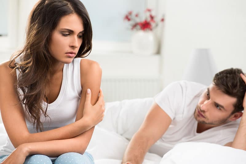 sad woman sitting next to her boyfriend on the bed
