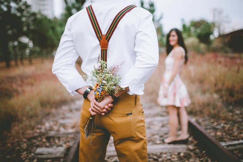 shallow focus back view of man holding flowers about to give his girlfriend