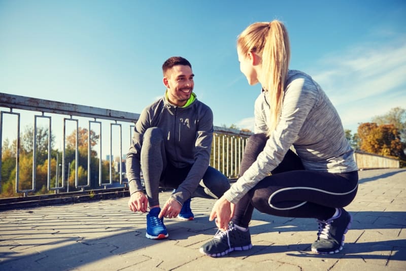 Una coppia sorridente si allaccia le scarpe per strada